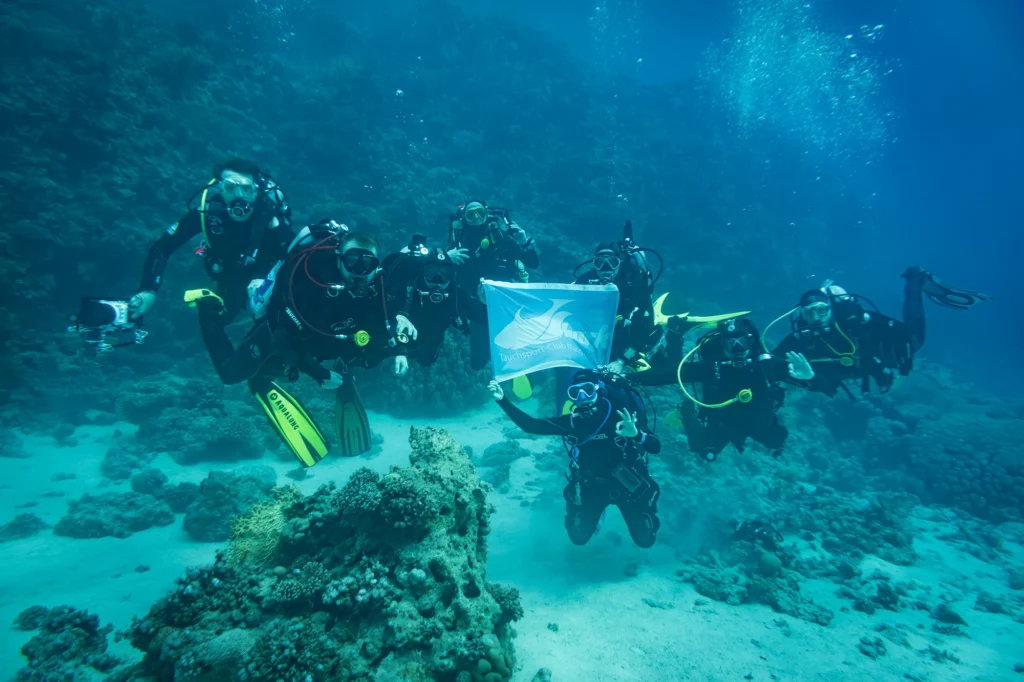 Taucherinnen und Taucher des TSC Shark Mannheim halten unter Wasser die Vereinsflagge